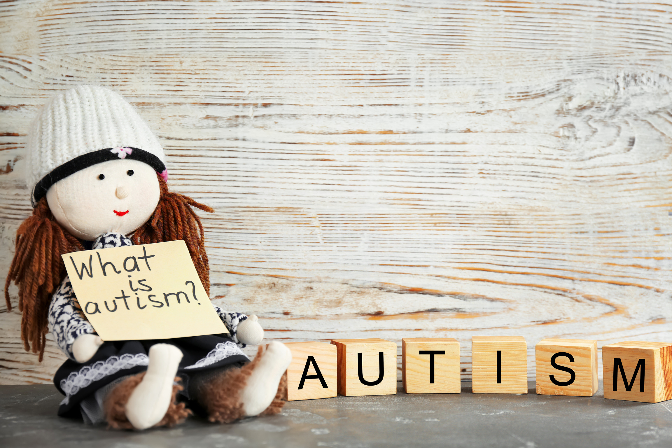 Doll Holding Note with Phrase "What Is Autism?" and Cubes on Table